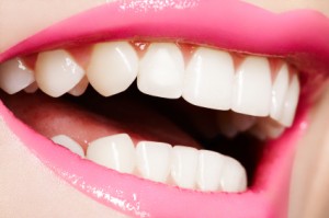 A woman smiling broadly with perfect teeth and pink lipstick.