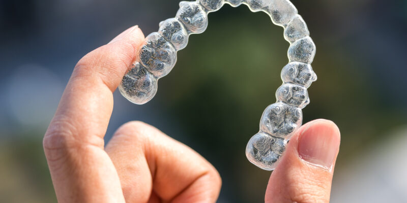 A clear aligner tray being held up between a person's fingers.