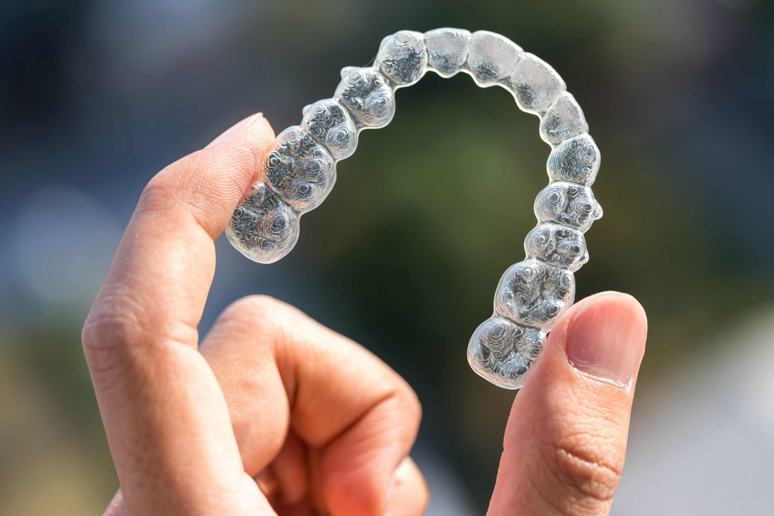 A clear aligner tray being held up between a person's fingers.