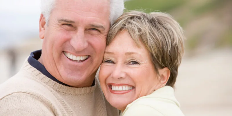 An elderly couple enjoying renewed smiles on the beach thanks to restorative dentistry in Loveland.